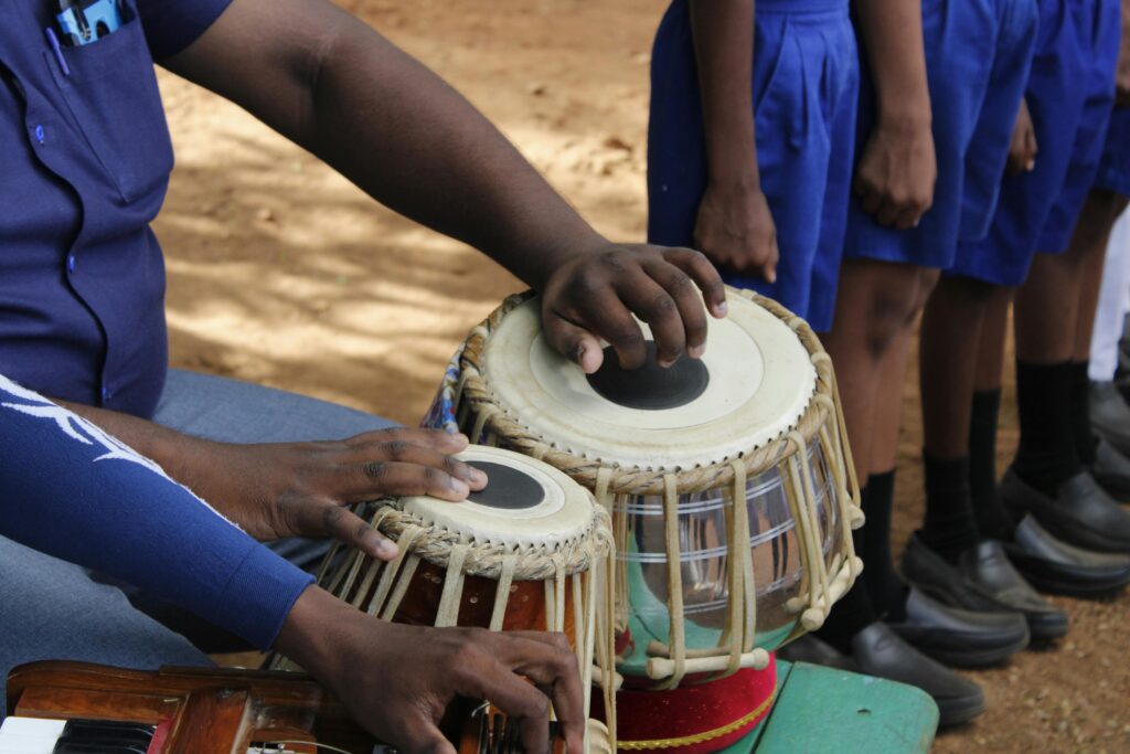 Musician playing tabla drums at a vibrant cultural event outdoors.